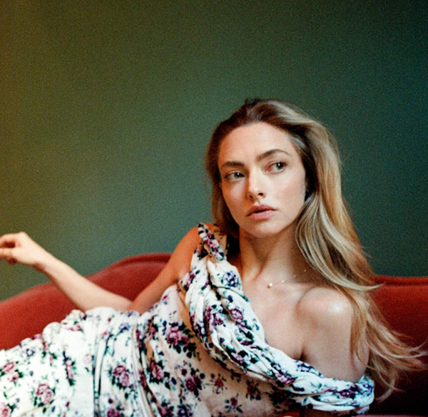 Amanda Seyfried in a floral dress lying on a red couch with a green background, brand 'MATEO' visible.
